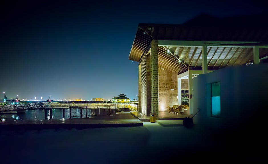 A modern waterfront house illuminated at night, featuring a serene cityscape and reflection on water.